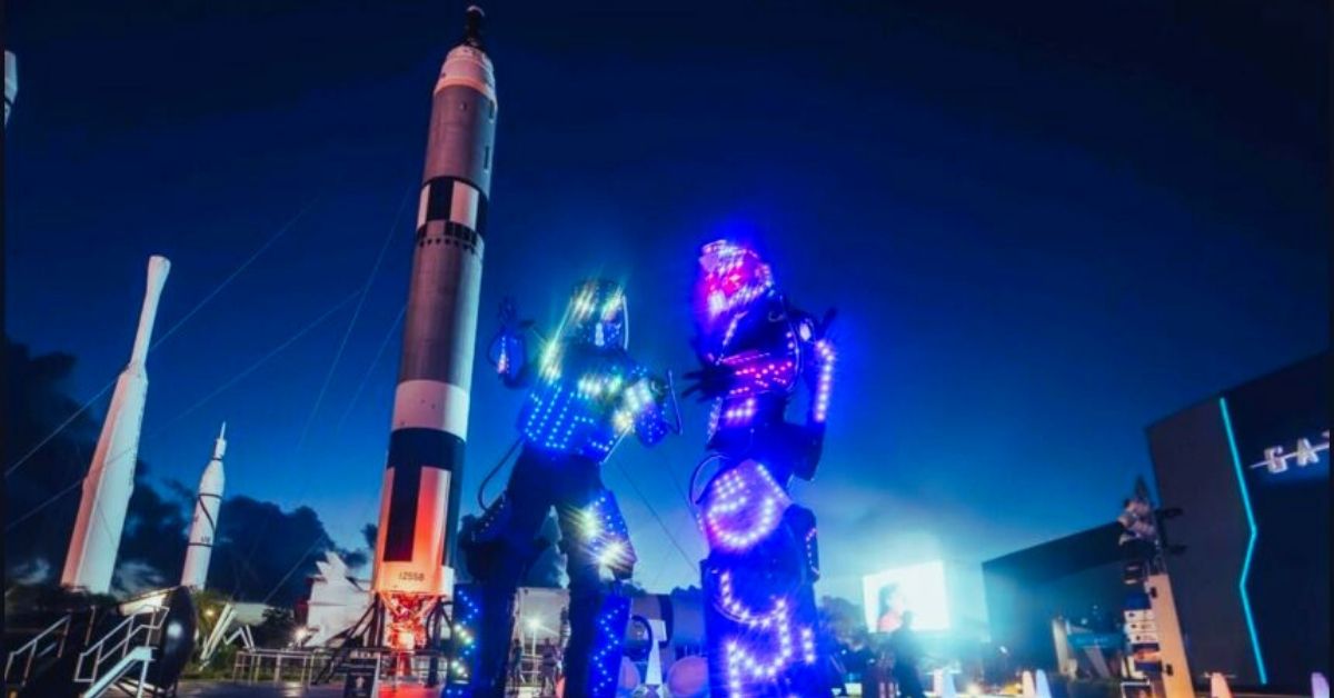 Performers com trajes de luz em frente a foguetes iluminados no evento Kennedy Under the Stars, no Kennedy Space Center