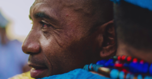 Homem com traje azul e colares coloridos é abraçado durante celebração da Festa de Iemanjá em Fortaleza.