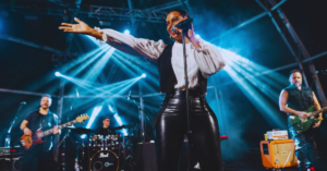 Cantora Alegria no palco durante tributo a Sade, com banda ao vivo e iluminação cênica colorida.