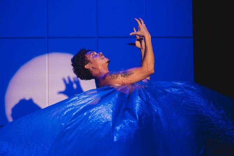 Silvero Pereira performando no palco com iluminação dramática durante a peça Pequeno Monstro.